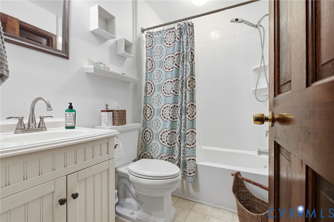 Bathroom featuring a beadboard vanity cabinet with a solid surface countertop, chrome dual-handle faucet, built-in wall shelving, and a shower-tub combination with white tile surround