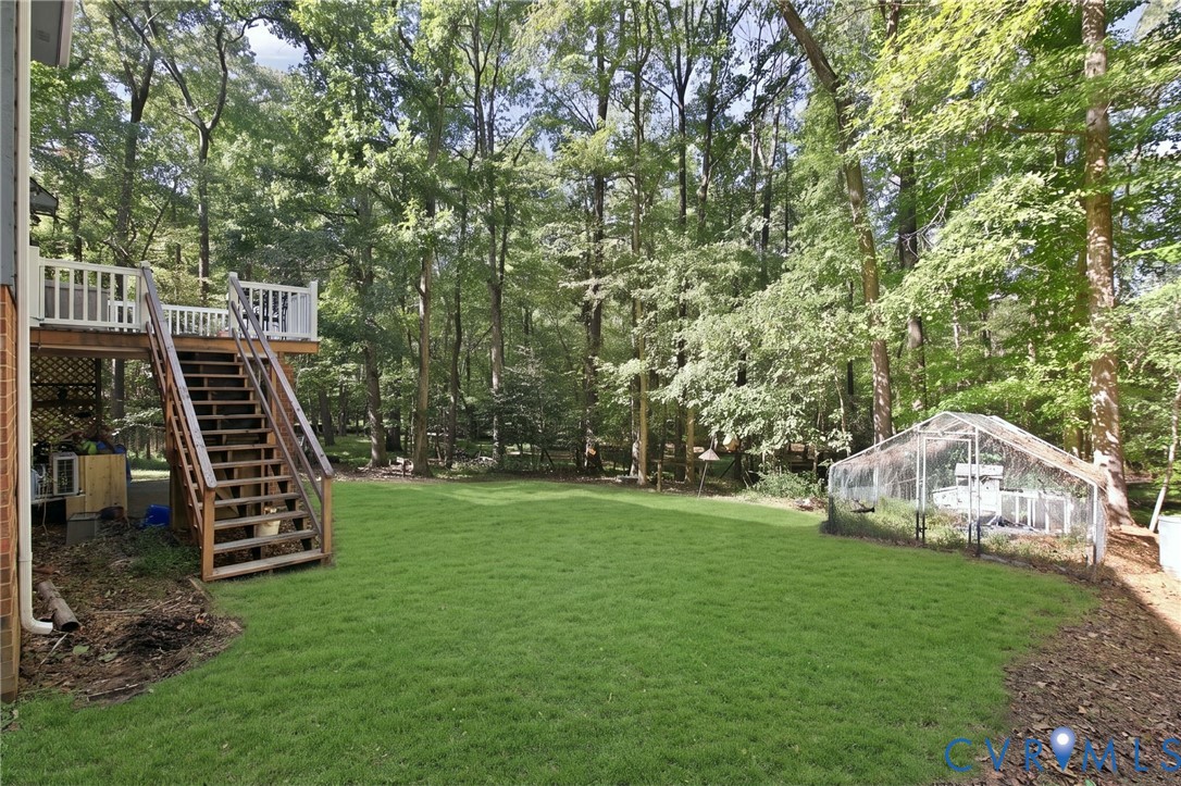 Expansive backyard featuring a tiered wooden deck with white railing, wood-frame staircase, manicured lawn, and mature woodland canopy