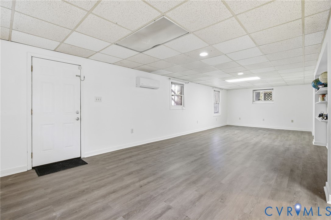 Finished space featuring wood-finish flooring, a suspended ceiling, built-in shelving, a wall-mounted ductless climate control unit, and recessed lighting
