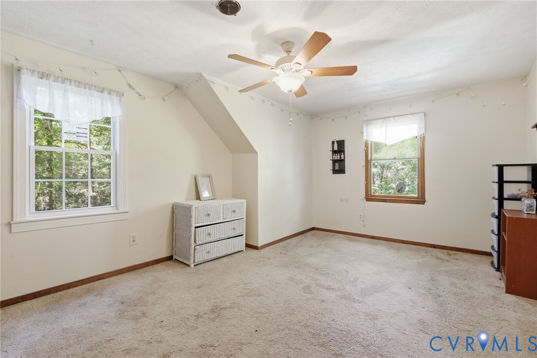 Room featuring neutral wall-to-wall carpeting, two double-hung windows with wood trim, and a ceiling fan with integrated lighting