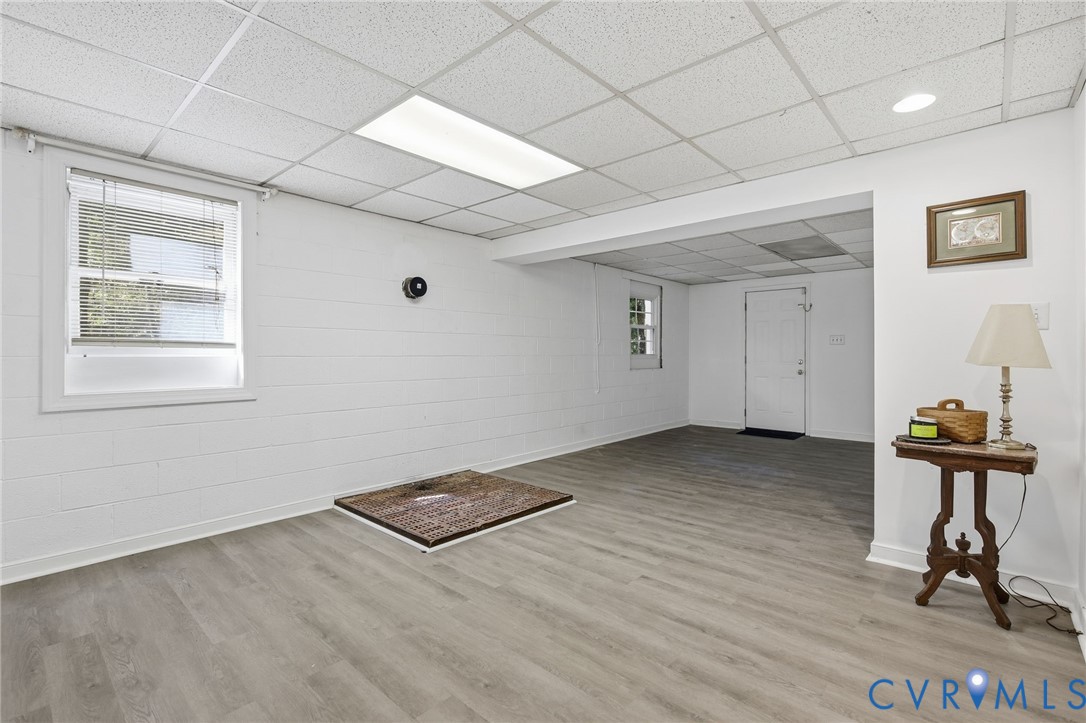 Finished interior space featuring wood-finish flooring, painted masonry walls, recessed drop-ceiling tiles, and multi-paned windows