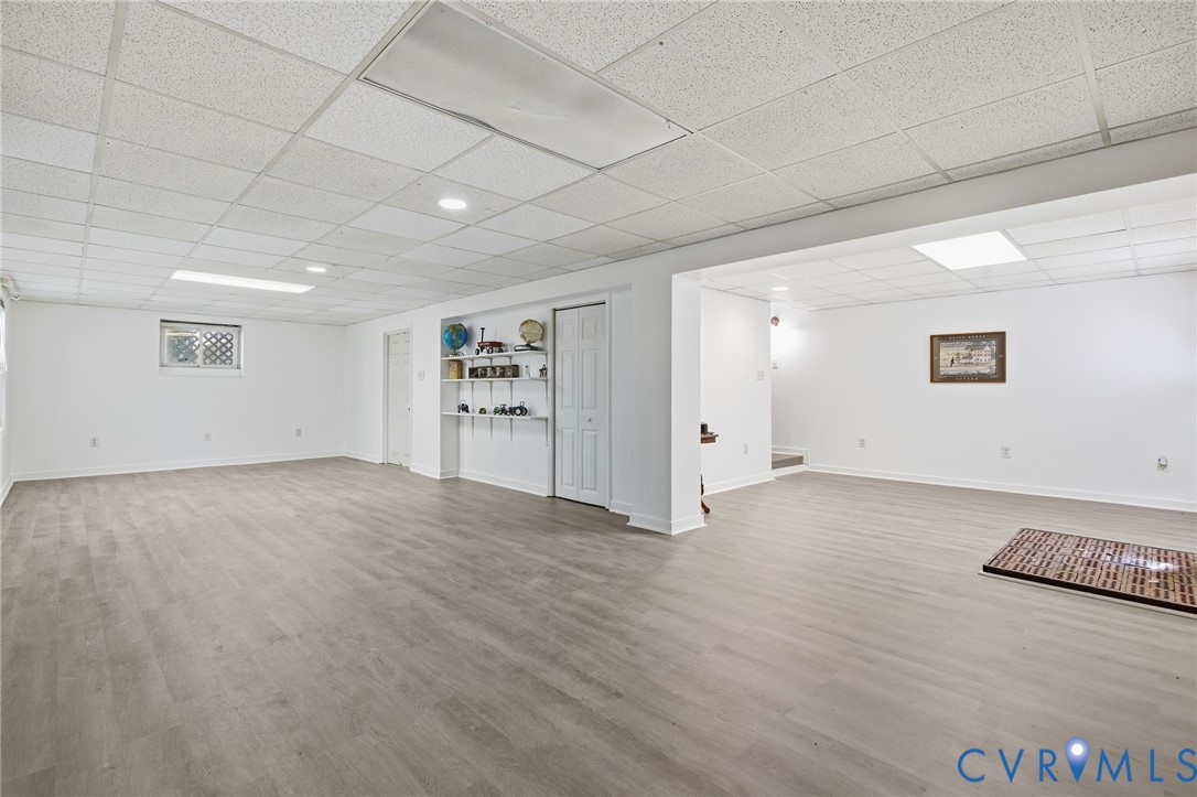 Expansive finished area featuring wood-finish flooring, a suspended acoustic tile ceiling, recessed lighting, and built-in wall shelving