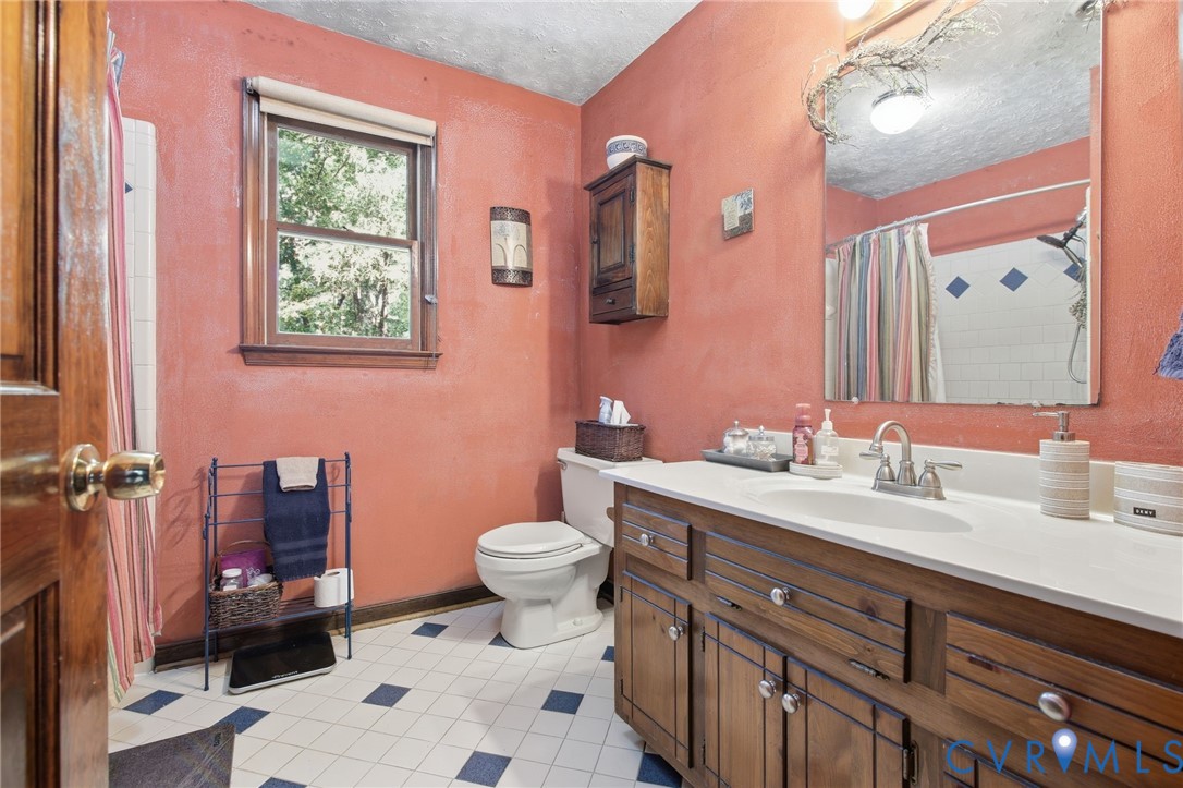 Bathroom featuring a solid wood vanity with integrated countertop, large wall-mounted mirror, ceramic tile flooring, and wood-framed window