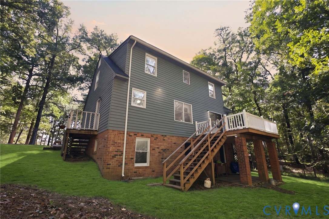 Exterior featuring a brick and horizontal siding faade, elevated rear wooden deck with white railing, and a sloped lawn surrounded by mature trees Exterior featuring a brick and horizontal siding faade, elevated rear wooden deck with white railing, and a sloped lawn surrounded by mature trees