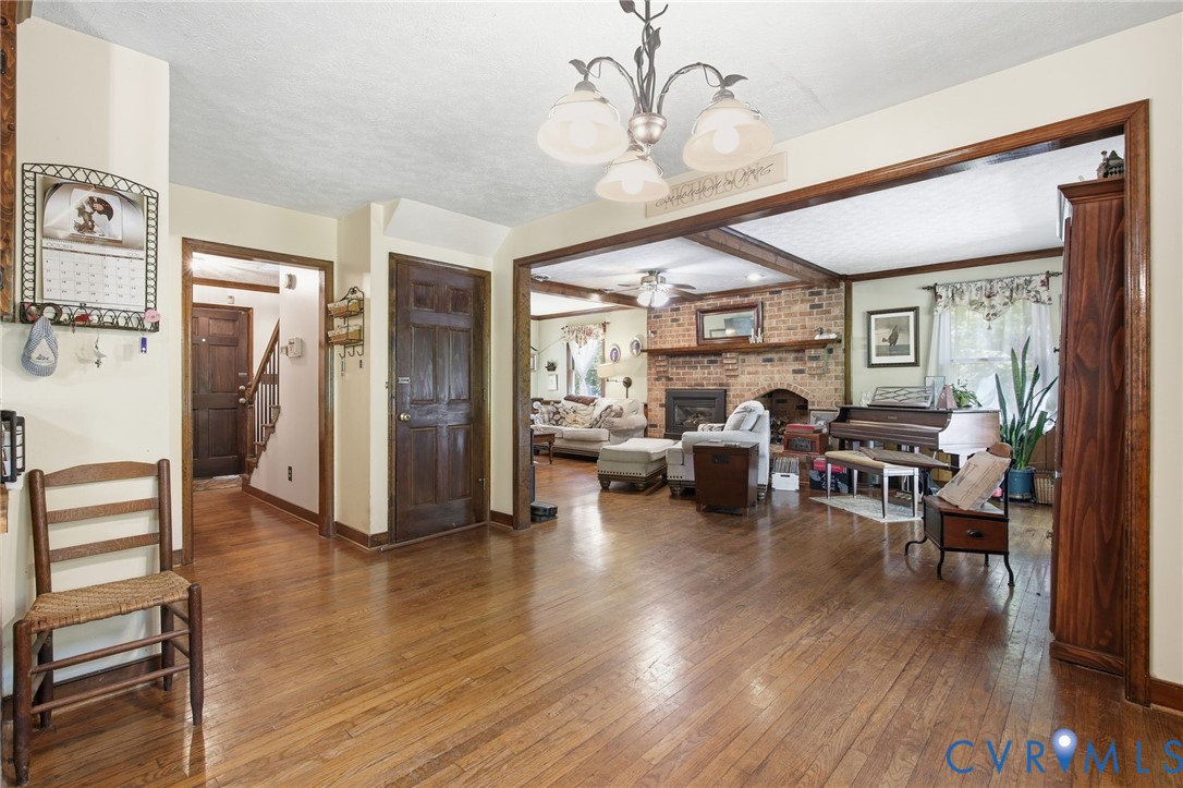 Wood flooring throughout, masonry fireplace with a brick surround and wood mantel, decorative chandelier, and stained wood door frames