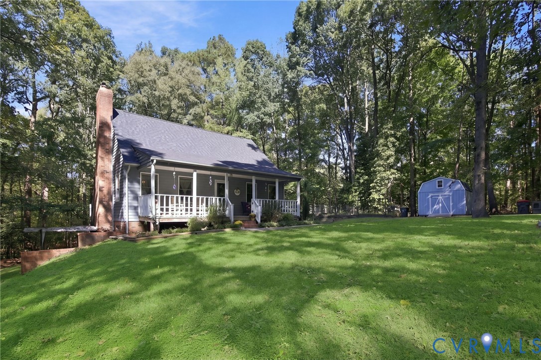 Exterior featuring a covered front porch, an external stone chimney, lap siding, and a detached storage structure set on a lot with mature trees Exterior featuring a covered front porch, an external stone chimney, lap siding, and a detached storage structure set on a lot with mature trees