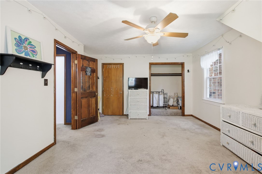 Carpeted room featuring a ceiling fan with light fixture, multi-pane window, and wood-finish interior doors