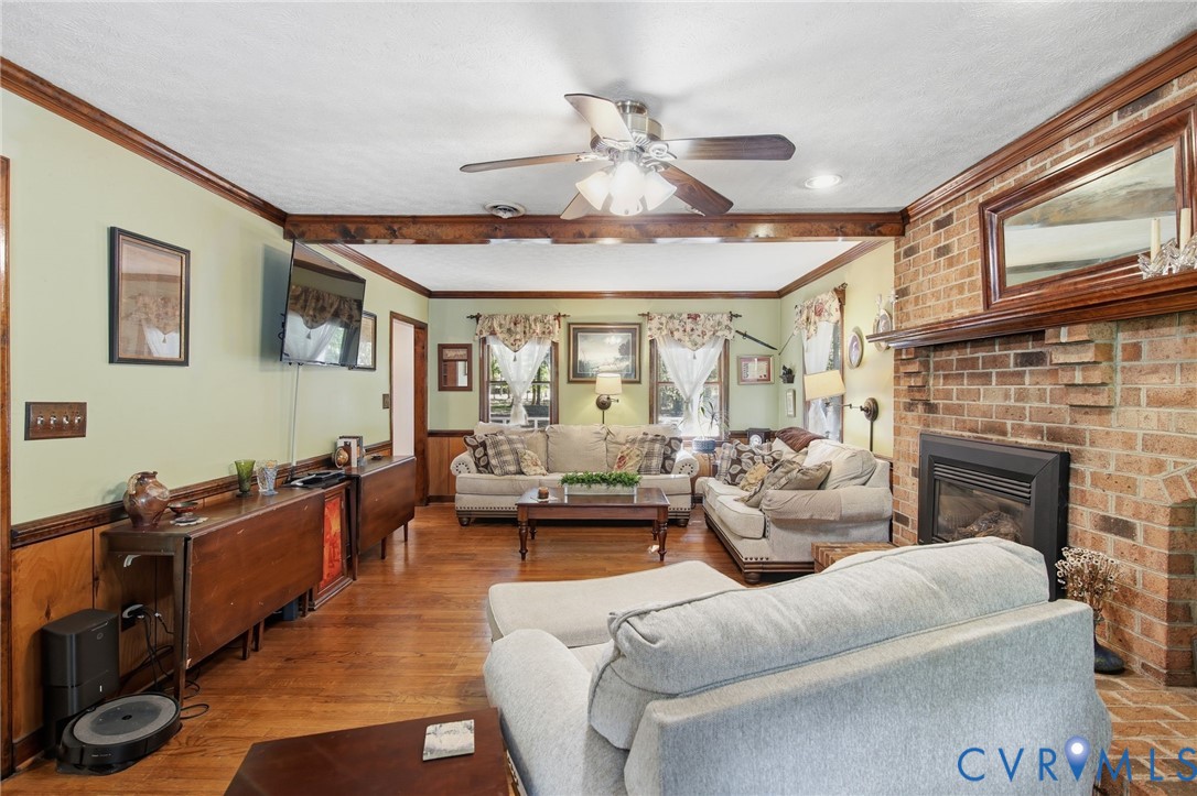 Hardwood flooring, wood-paneled wainscoting, exposed ceiling beams, and a floor-to-ceiling brick fireplace with a wood mantel Hardwood flooring, wood-paneled wainscoting, exposed ceiling beams, and a floor-to-ceiling brick fireplace with a wood mantel