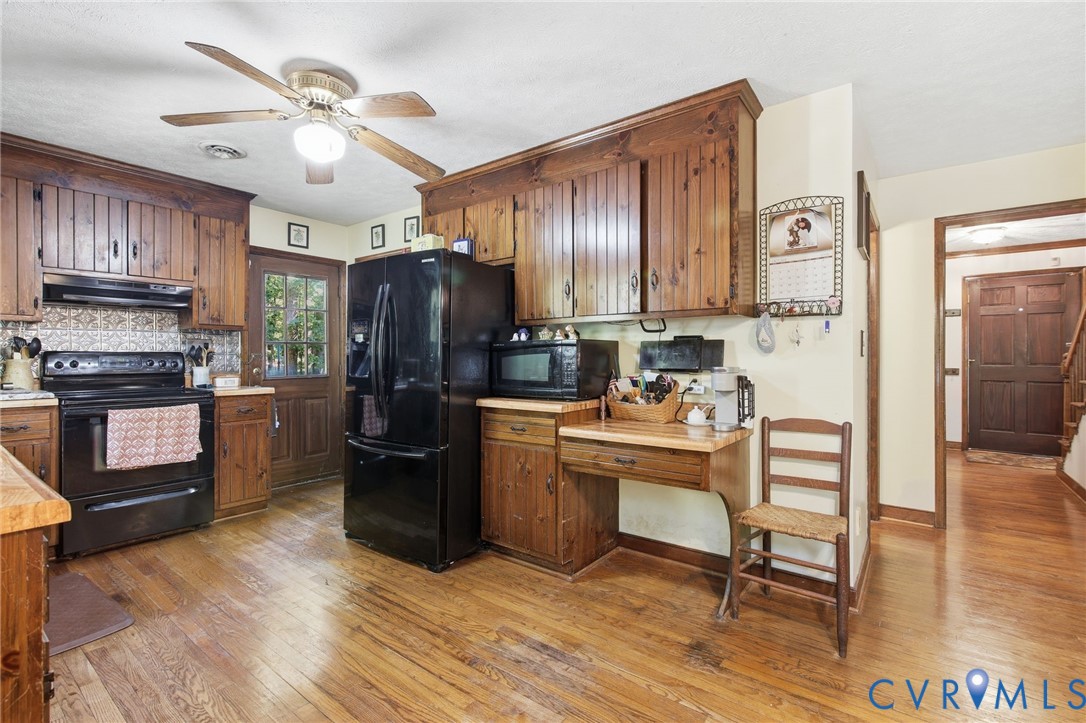 Kitchen featuring solid wood cabinetry, black appliances, a built-in desk area, and wood flooring Kitchen featuring solid wood cabinetry, black appliances, a built-in desk area, and wood flooring