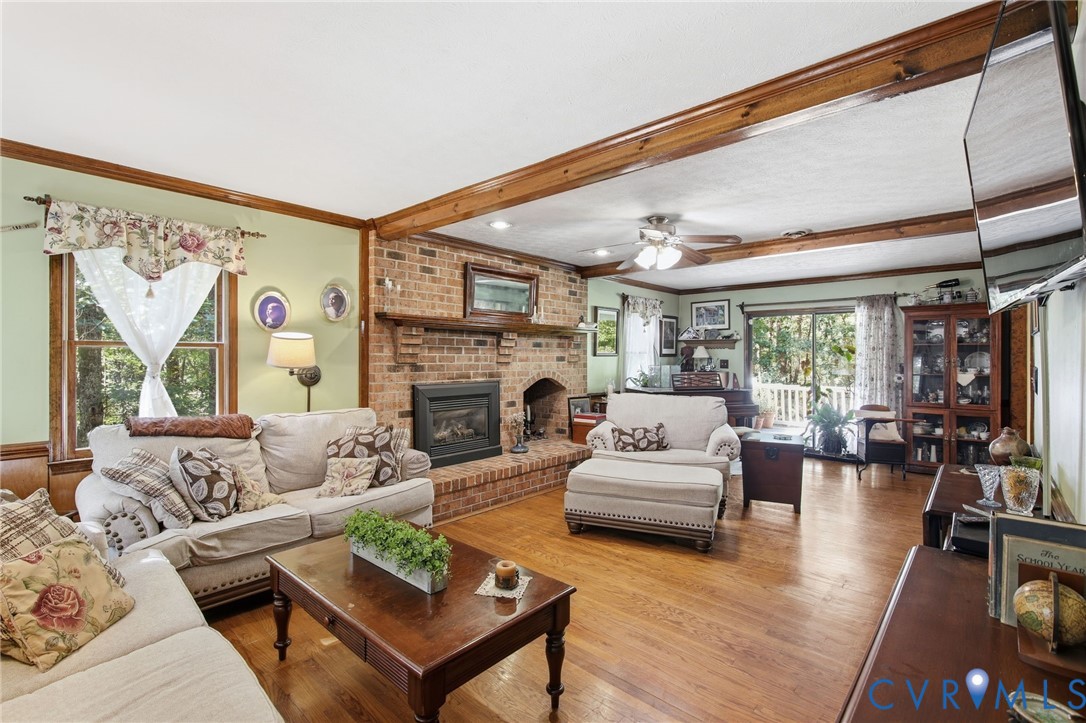 Living area featuring exposed ceiling beams, wood-finish flooring, and a floor-to-ceiling brick fireplace with a built-in mantle Living area featuring exposed ceiling beams, wood-finish flooring, and a floor-to-ceiling brick fireplace with a built-in mantle