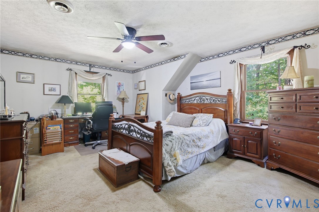 Bedroom featuring carpeted flooring, a ceiling fan, and large windows with decorative border detailing