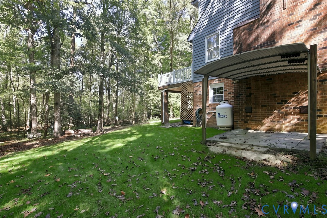 Backyard featuring a paved patio with a corrugated metal cover, an elevated wood-railing deck, red brick and horizontal siding exterior, and mature trees