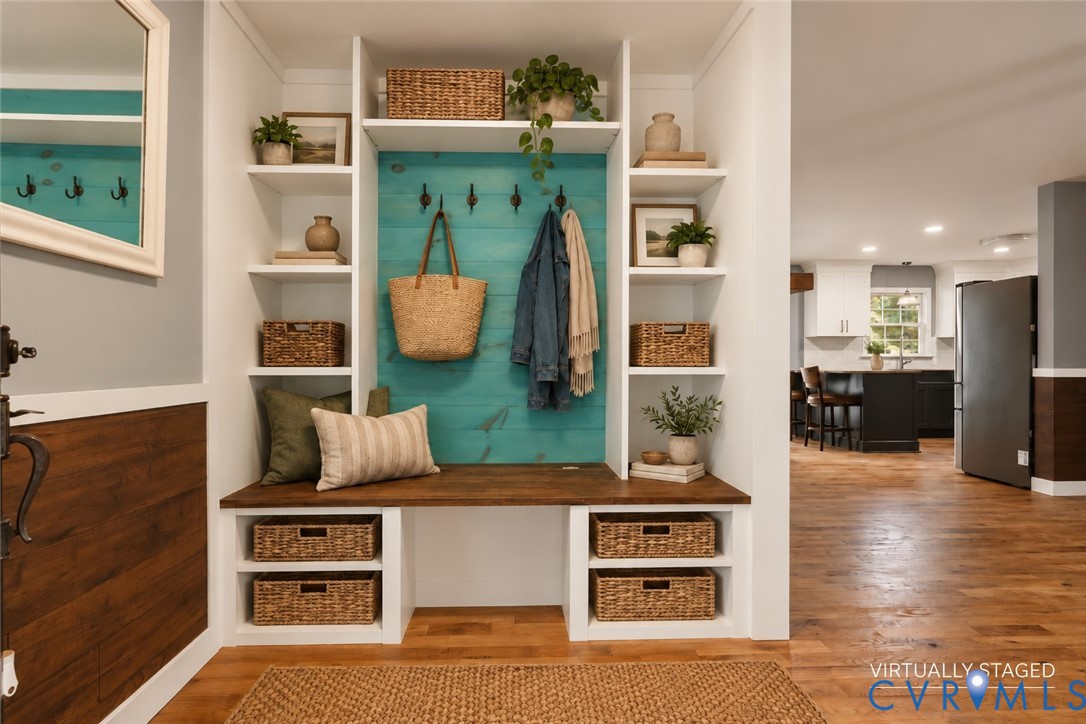 Built-in mudroom organization featuring white cabinetry, a wood-finish bench, matte black hardware, and wood-finish flooring