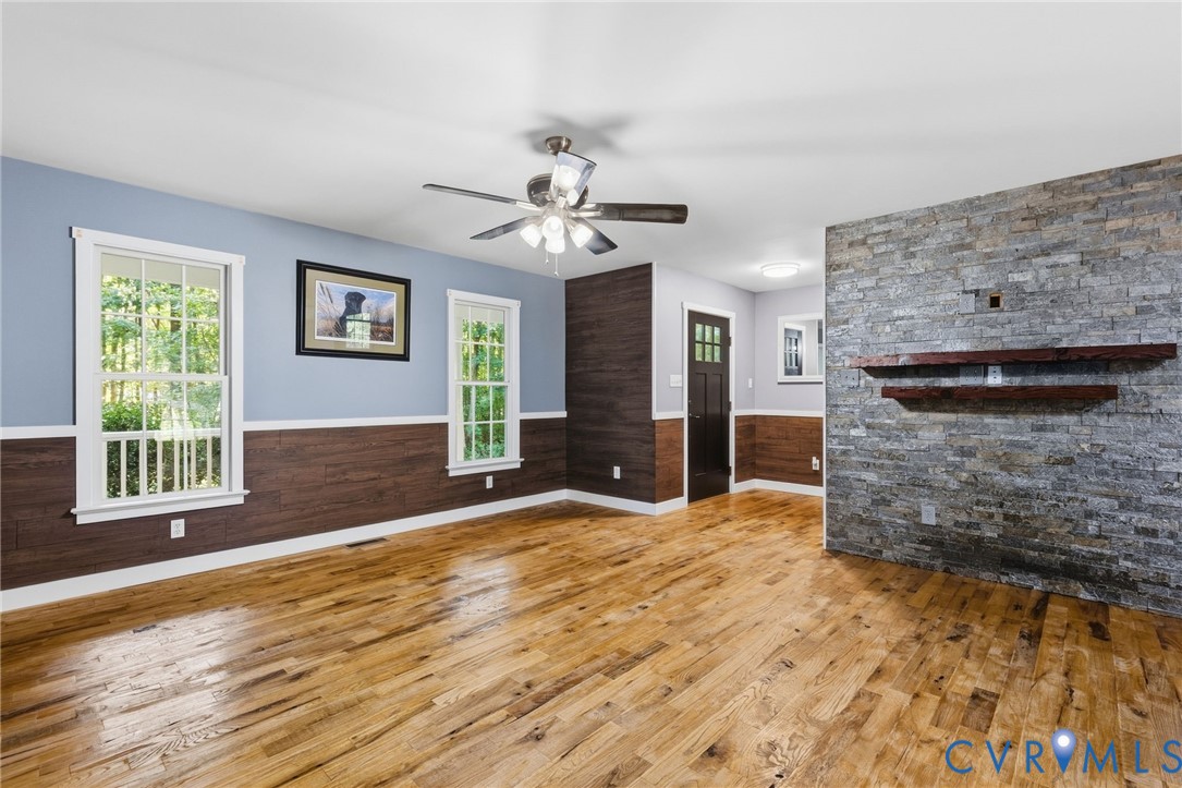 Living area featuring wood-finish flooring, stone-veneer accent wall, horizontal wood-panel wainscoting, and a ceiling-mounted light fixture with a fan
