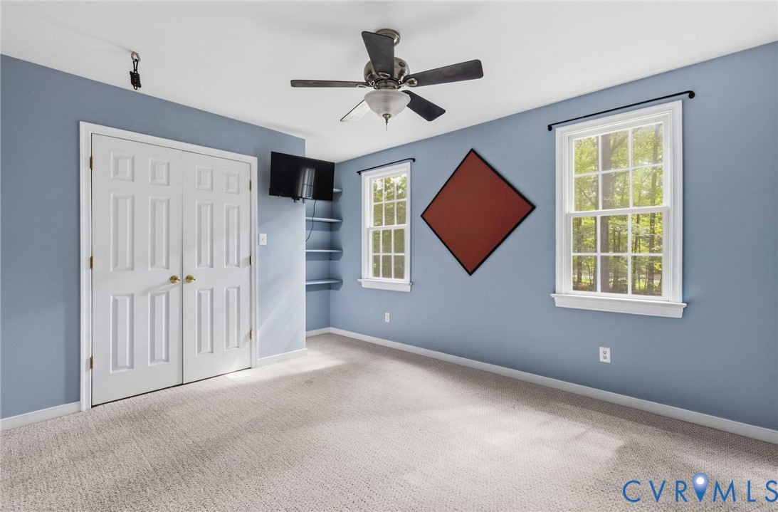 Room featuring wall-to-wall carpeting, dual-pane windows, built-in corner shelving, and a ceiling fan with integrated lighting