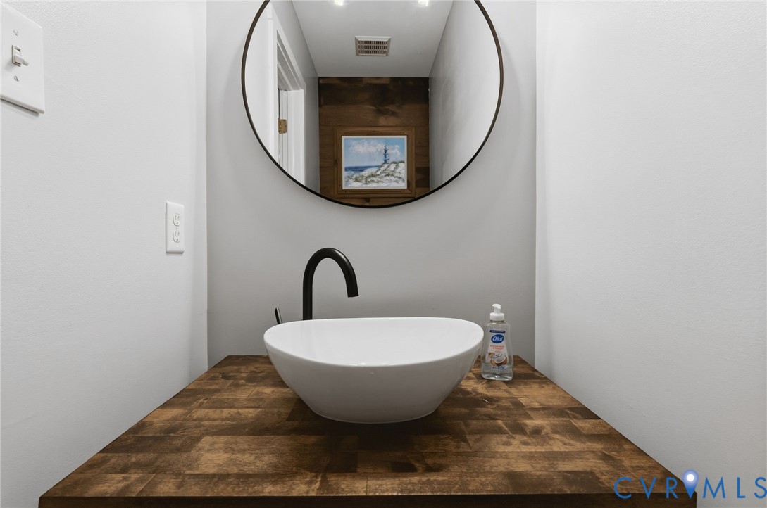 Floating vanity featuring a wood-block countertop, white vessel sink, matte black faucet, and circular wall-mounted mirror