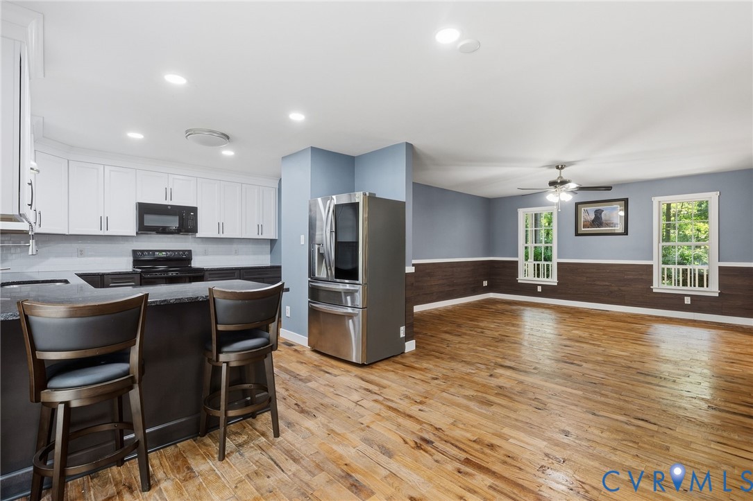 Kitchen featuring white shaker-style cabinetry, a dark-toned breakfast bar, wood-finish flooring, wainscoting, and recessed lighting Kitchen featuring white shaker-style cabinetry, a dark-toned breakfast bar, wood-finish flooring, wainscoting, and recessed lighting
