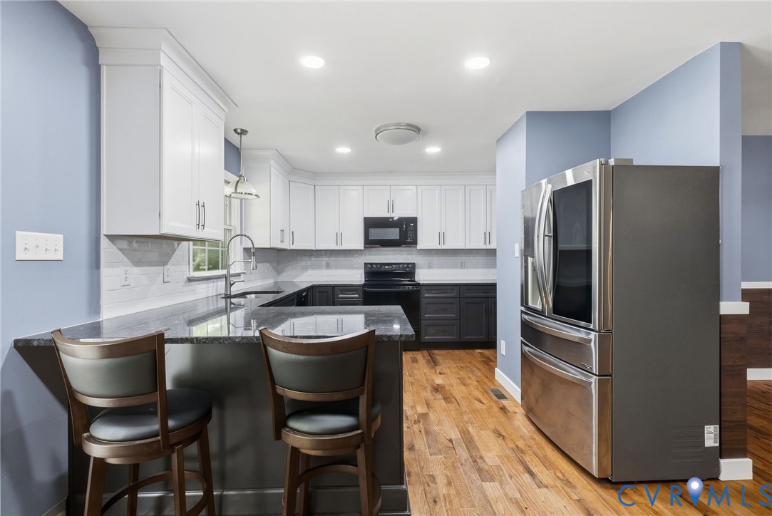 Kitchen featuring two-tone cabinetry, stone-surface countertops, recessed lighting, wood-finish flooring, and stainless steel appliances Kitchen featuring two-tone cabinetry, stone-surface countertops, recessed lighting, wood-finish flooring, and stainless steel appliances