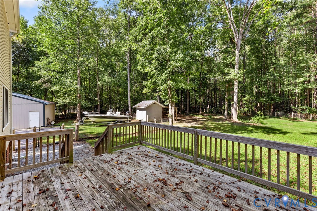 Raised wood deck with a picket railing, expansive lawn, detached storage structure, and perimeter mature trees