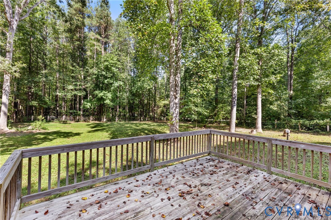 Elevated wood deck with perimeter railing overlooking a backyard featuring a lawn and mature trees