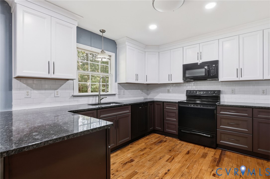 Kitchen featuring white upper and dark lower cabinetry, stone countertops, a subway tile backsplash, and wood-finish flooring Kitchen featuring white upper and dark lower cabinetry, stone countertops, a subway tile backsplash, and wood-finish flooring