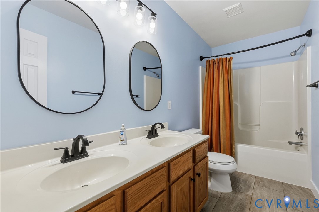 Double vanity featuring wood cabinetry, solid-surface countertops with dual integrated sinks, matte black fixtures, and two oval wall-mounted mirrors
