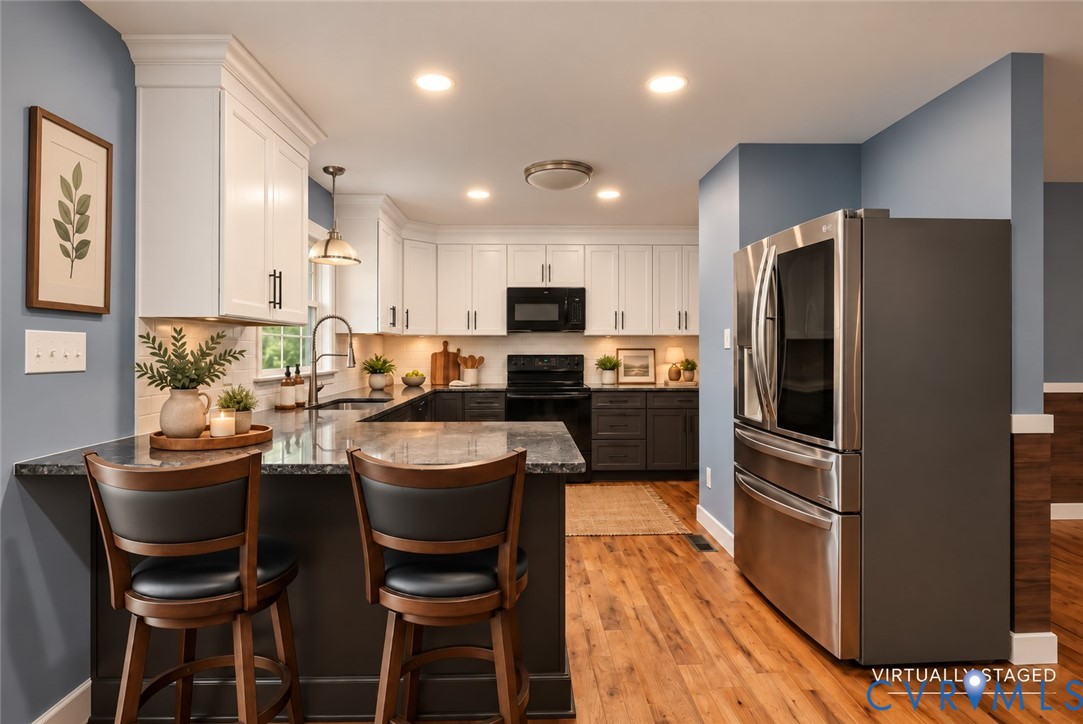 Kitchen featuring white upper cabinetry, dark lower cabinetry, stone-surface countertops, wood-finish flooring, and stainless steel refrigerator Kitchen featuring white upper cabinetry, dark lower cabinetry, stone-surface countertops, wood-finish flooring, and stainless steel refrigerator