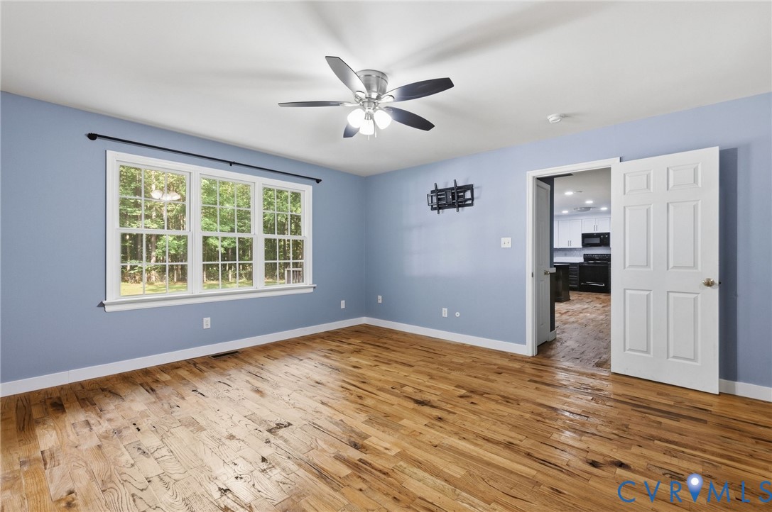 Wood-finish flooring, multi-pane windows, and a multi-blade ceiling fan with integrated lighting