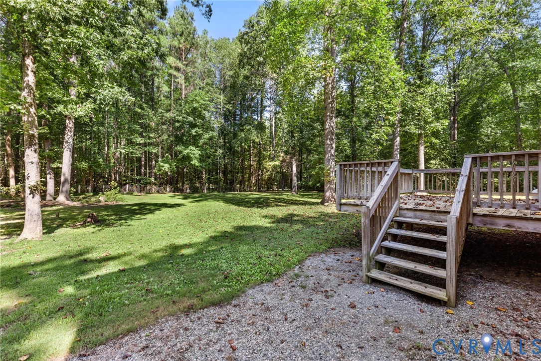 Spacious backyard featuring a wood deck with stairs, graveled ground area, grass lawn, and mature trees