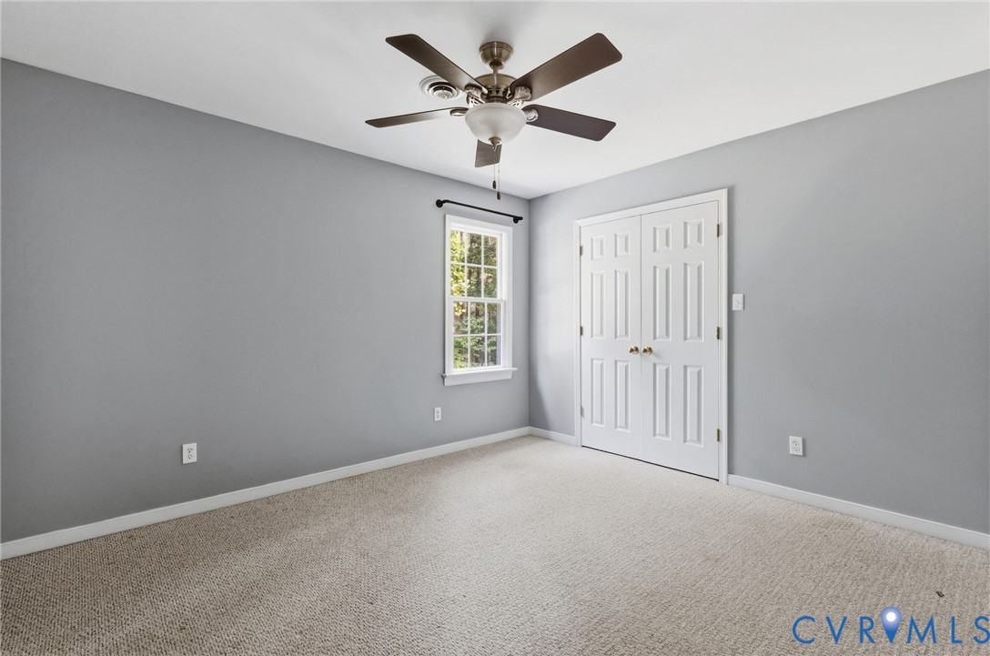 Neutral-toned interior space featuring wall-to-wall carpeting, a multi-pane window, double-panel closet doors, and a ceiling-mounted fan with integrated lighting