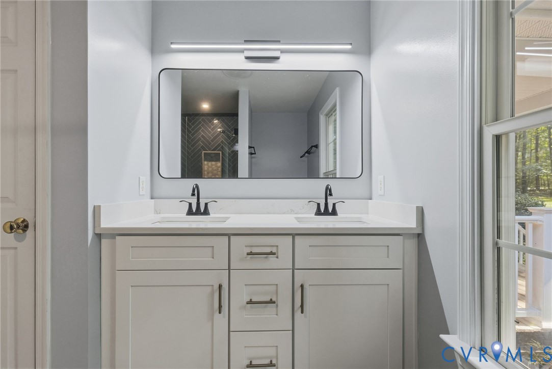 Dual-vanity cabinetry with a light finish, quartz countertop, rectangular under-mount sinks, matte black hardware, and an elongated linear light fixture