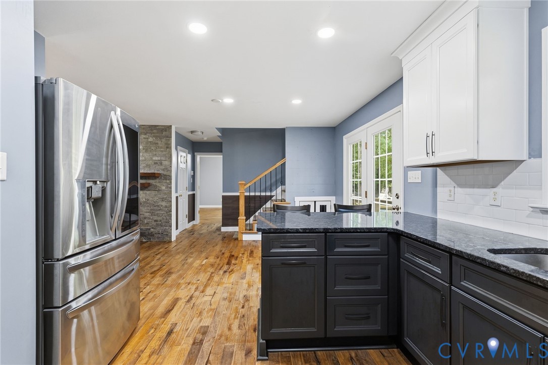 Kitchen featuring two-tone cabinetry, stone countertops, stainless steel refrigerator, recessed lighting, and wood-finish flooring Kitchen featuring two-tone cabinetry, stone countertops, stainless steel refrigerator, recessed lighting, and wood-finish flooring