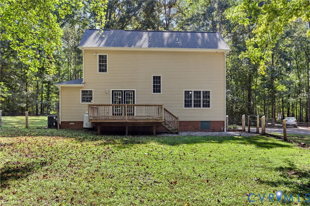 Exterior featuring beige vinyl siding, a rear wooden deck with stairs, a brick foundation base, and multiple multi-pane windows