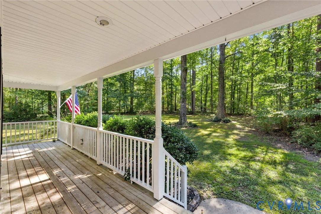 Covered front porch featuring wood-plank flooring, white decorative railings, and a beadboard ceiling with recessed lighting, overlooking a wooded lot