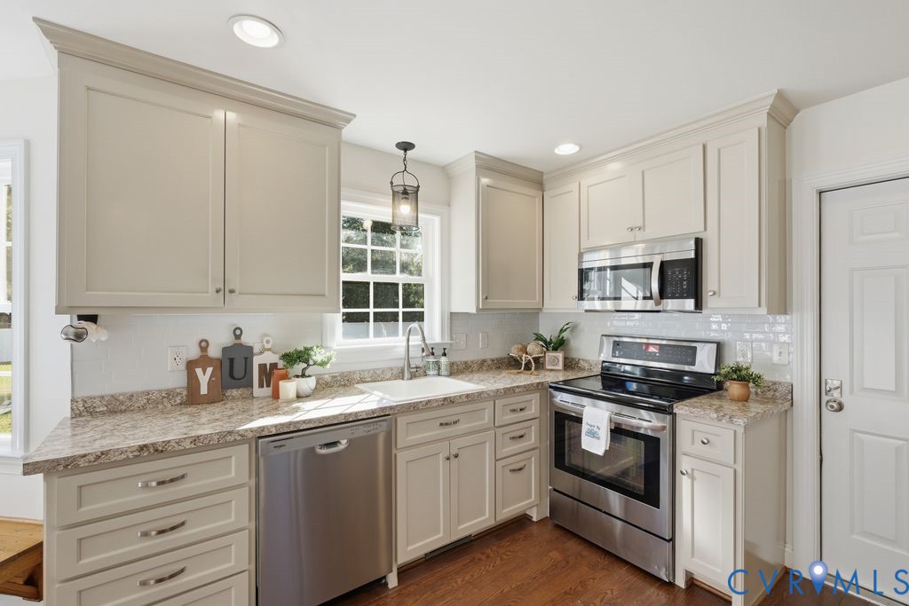 Kitchen featuring shaker-style cabinetry, patterned stone-look countertops, stainless steel appliances, white subway tile backsplash, and wood-finish flooring