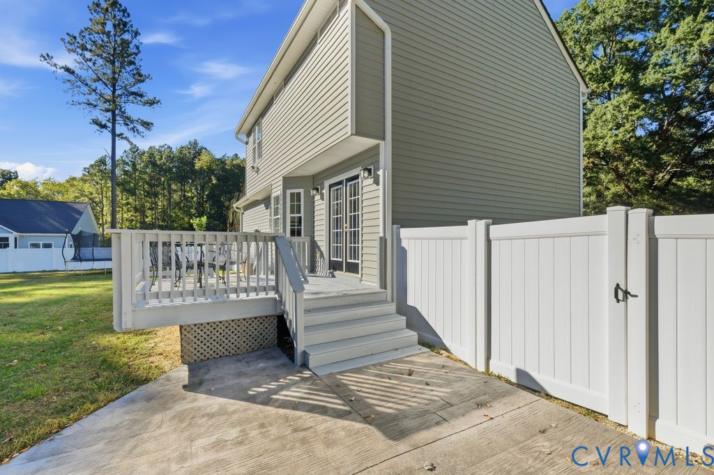 Exterior featuring neutral-toned siding, a raised wooden deck with railings, concrete patio space, and a white privacy fence