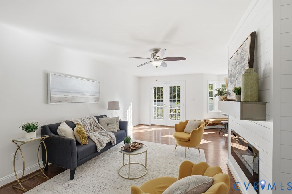 Living area featuring a horizontal fireplace with a custom mantel, wood-finish flooring, a ceiling fan, a multi-pane glass-paneled exterior door, and a bay window