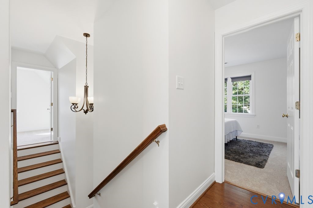 Hallway featuring wood-finish flooring, a metal multi-light chandelier, and a wood-finish handrail