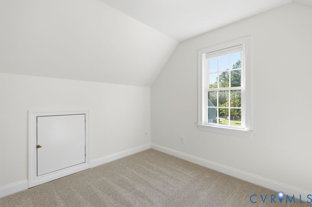 Room featuring neutral-toned carpeting, slanted ceilings, a single-hung window with a grille pattern, and a built-in access panel