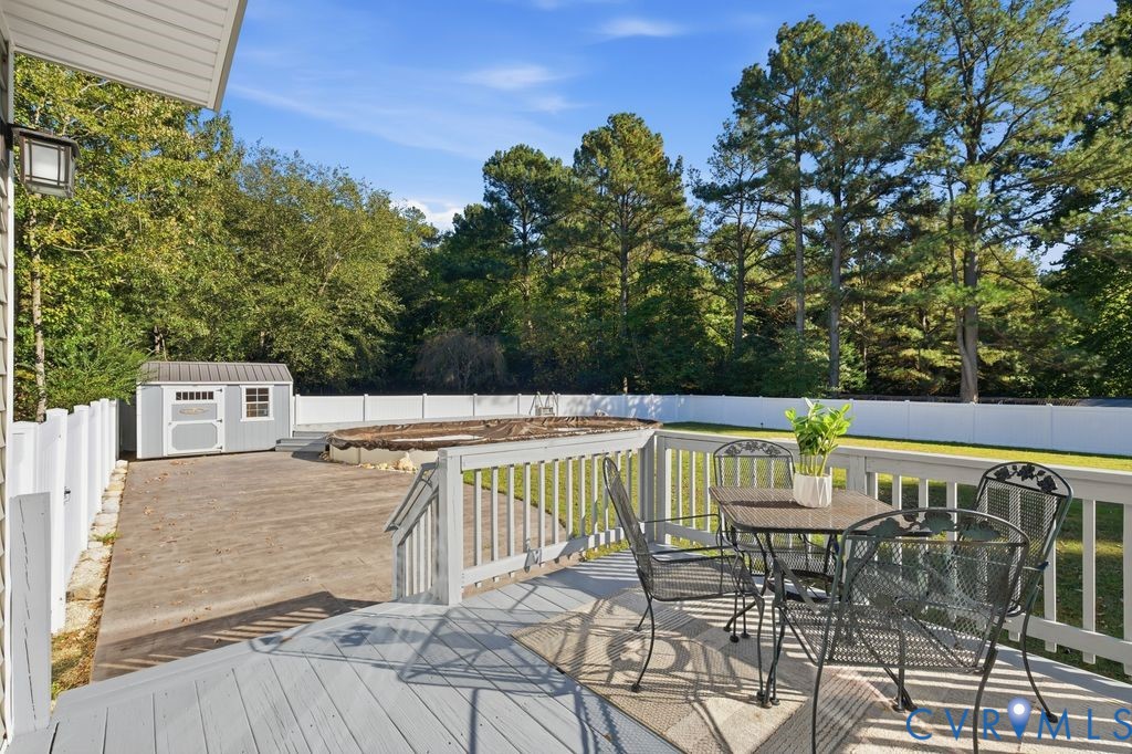 Elevated wood deck featuring a railing system, expansive fenced backyard, detached storage building, and an above-ground pool