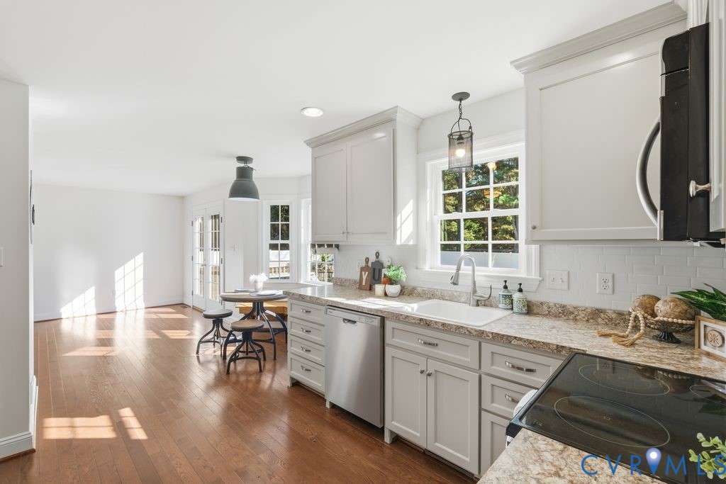 Kitchen featuring shaker-style cabinetry, stone-finish countertops, stainless steel appliances, wood-finish flooring, and a subway tile backsplash