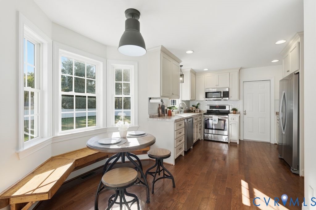 Kitchen featuring wood-finish flooring, built-in cabinetry, stainless steel appliances, a built-in wooden dining bench, and a bay window