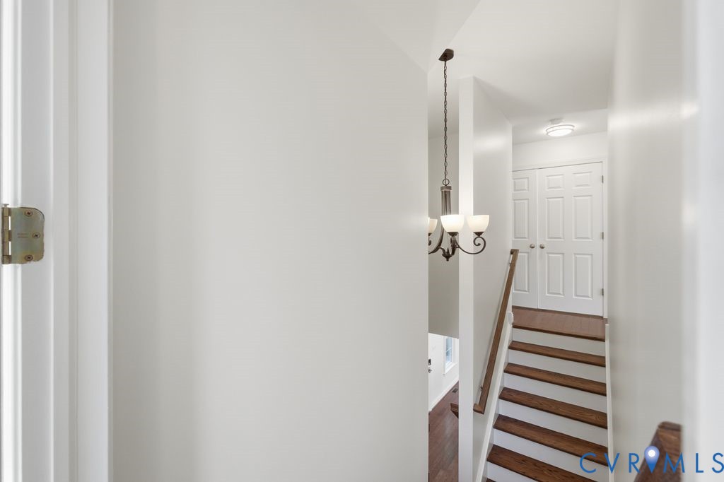 Staircase featuring wood-finish treads, painted risers, and a metal handrail, illuminated by a multi-light chandelier and a flush-mount ceiling light, with double-panel doors