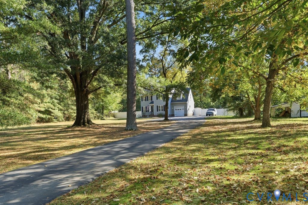 Two-story residence featuring a paved driveway, attached garage, and white privacy fencing set within a lot with mature trees