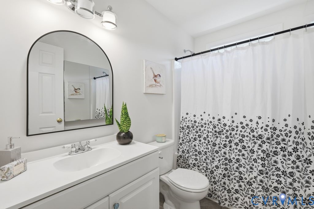 Bathroom featuring a white vanity with a solid-surface countertop, an arched-top mirror, and a three-light wall-mounted fixture