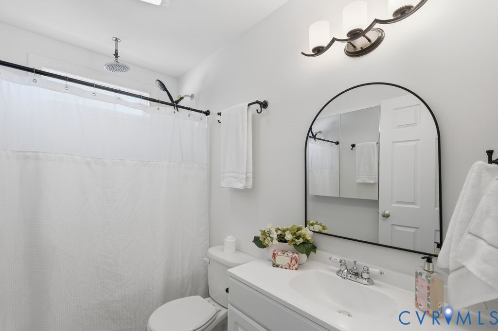 Bathroom featuring a vanity with a countertop basin, arched wall-mounted mirror, rain shower head, three-light fixture, and matte black hardware