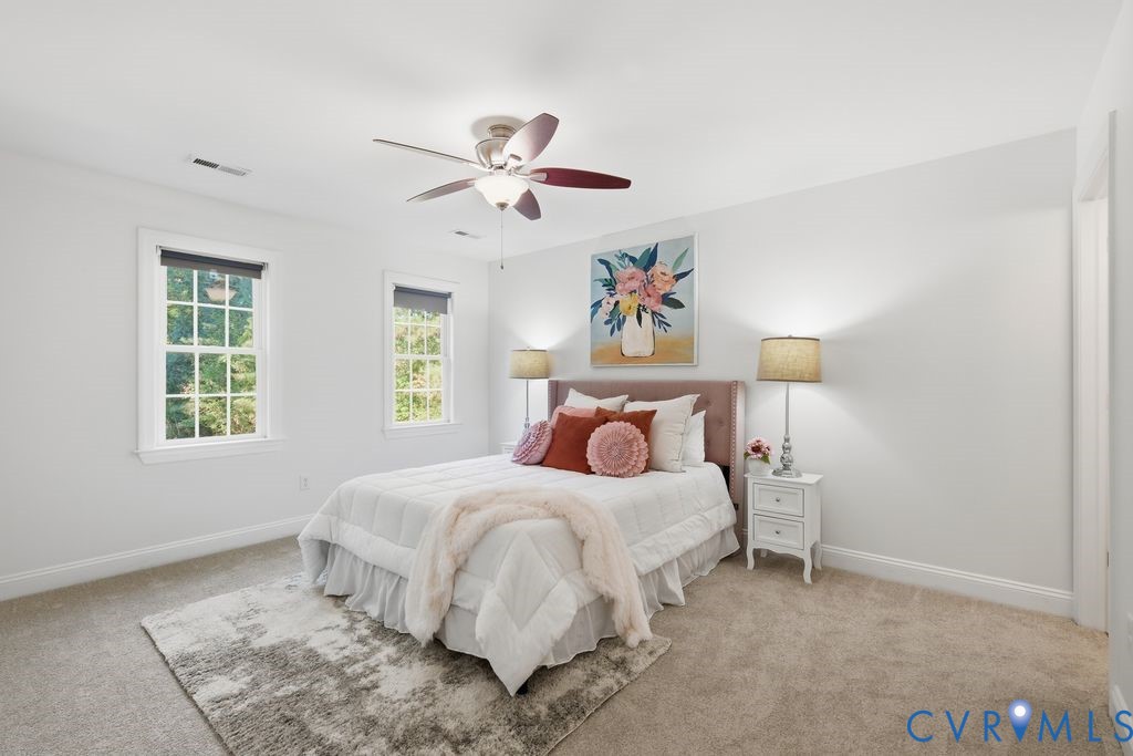 Neutral-toned interior featuring wall-to-wall carpeting, multiple double-hung windows with exterior trim, and a ceiling-mounted light fixture with a multi-blade fan