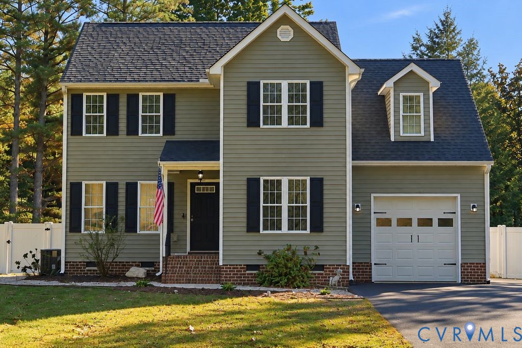Two-story residence featuring sage green siding, contrasting dark shutters, a brick foundation facade, an attached garage with window inserts, and a gable roofline