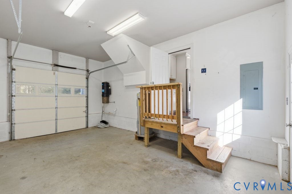 Two-car garage featuring a sectional overhead door, built-in central vacuum system, dual flush-mount fluorescent lighting, and a raised wooden staircase with balustrade