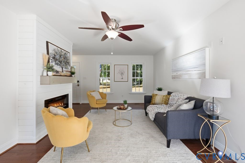 Interior space featuring wood-finish flooring, a white shiplap fireplace surround with a mantel, multi-pane windows, and a ceiling fan with integrated lighting